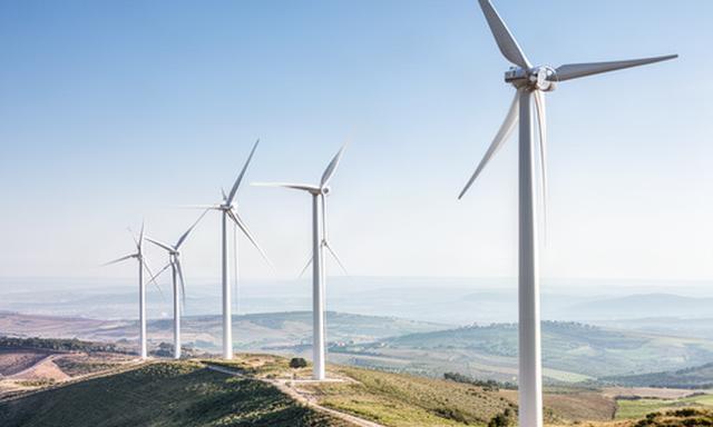 Aerogeneradores blancos alineados en una loma de Cataluña bajo un cielo azul y viento constante